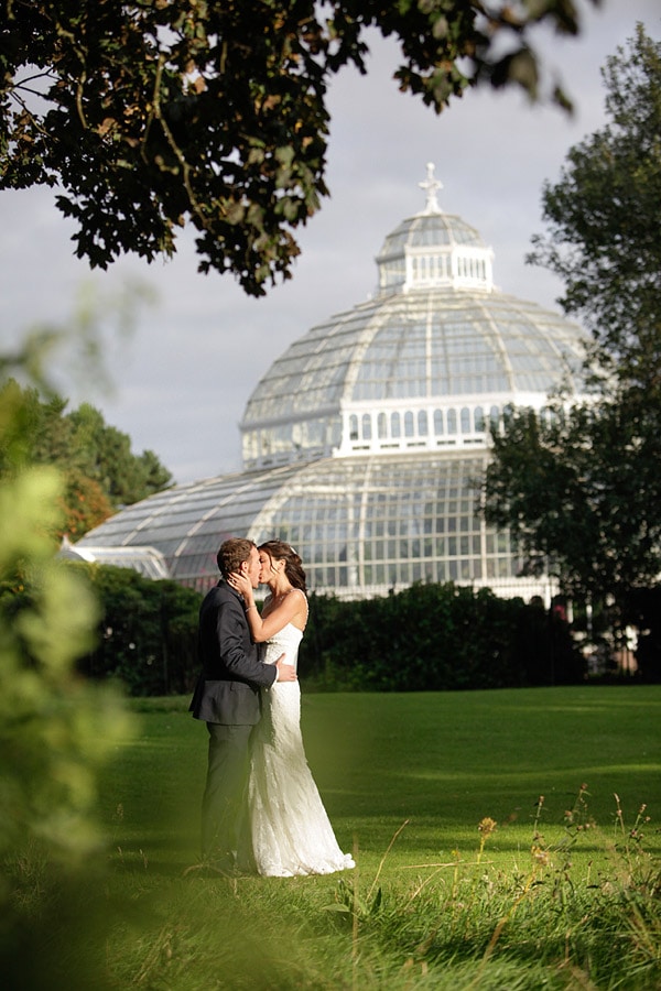 palm house wedding photos, couple kiss with the palm house in the background.