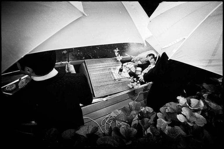 documentary weddings photography example showing the couple kissing under umbrellas on a boat as rain falls.
