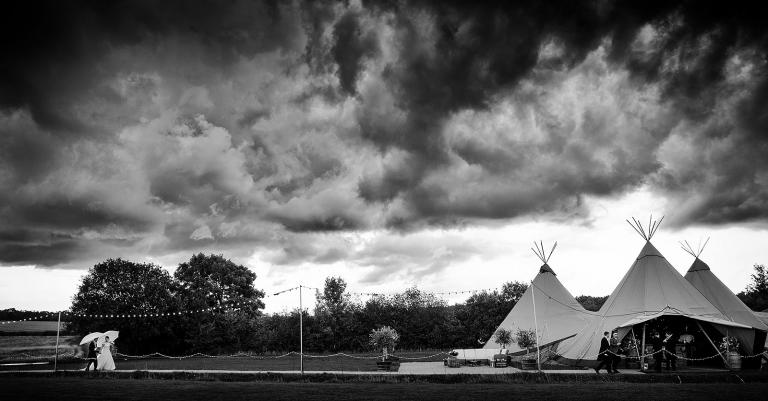 Storm clouds with the bride and groom with umbrellas